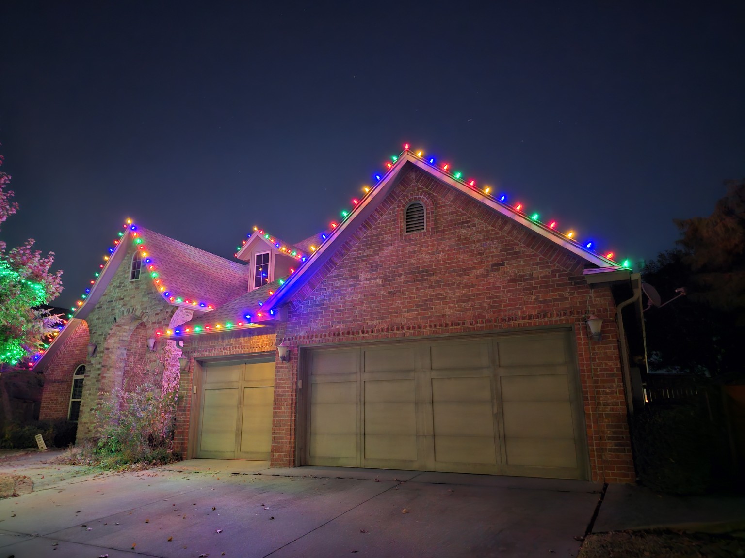 Multicolor lights outlining a brick home's roof and dormer