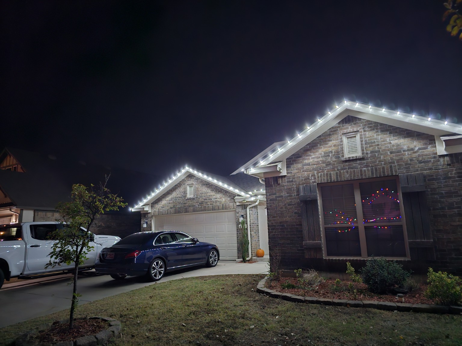 White Christmas lights outlining a brick home's roofline at night